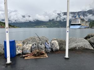 Søppelsekkar på kaikanten, cruiseskip i bakgrunnen